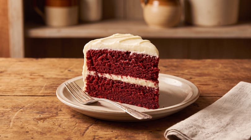 A slice of red velvet cake with cream cheese frosting on a plate with a fork and napkin.
